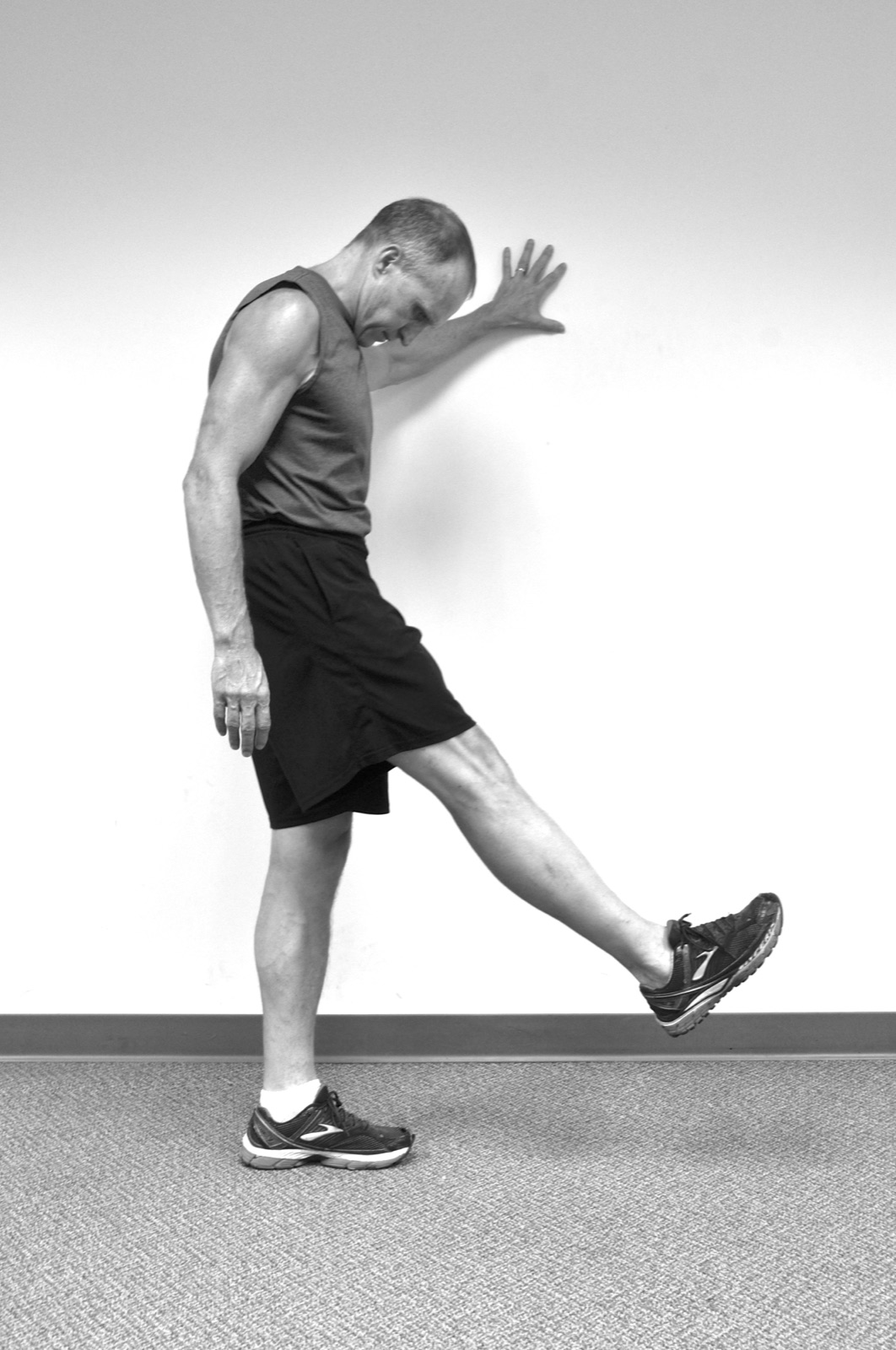 Person standing with one hand against a wall while extending one leg forward.